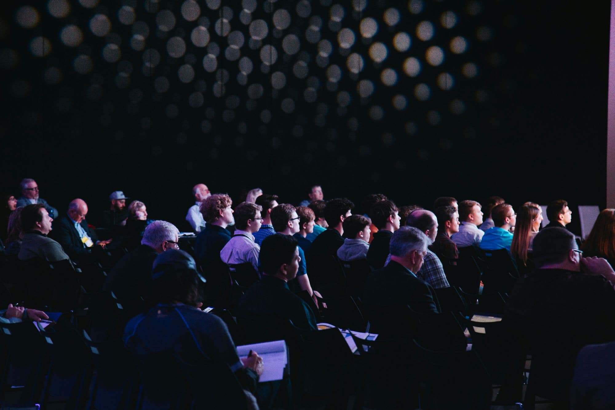 A darkened auditorium audience facing a lit stage