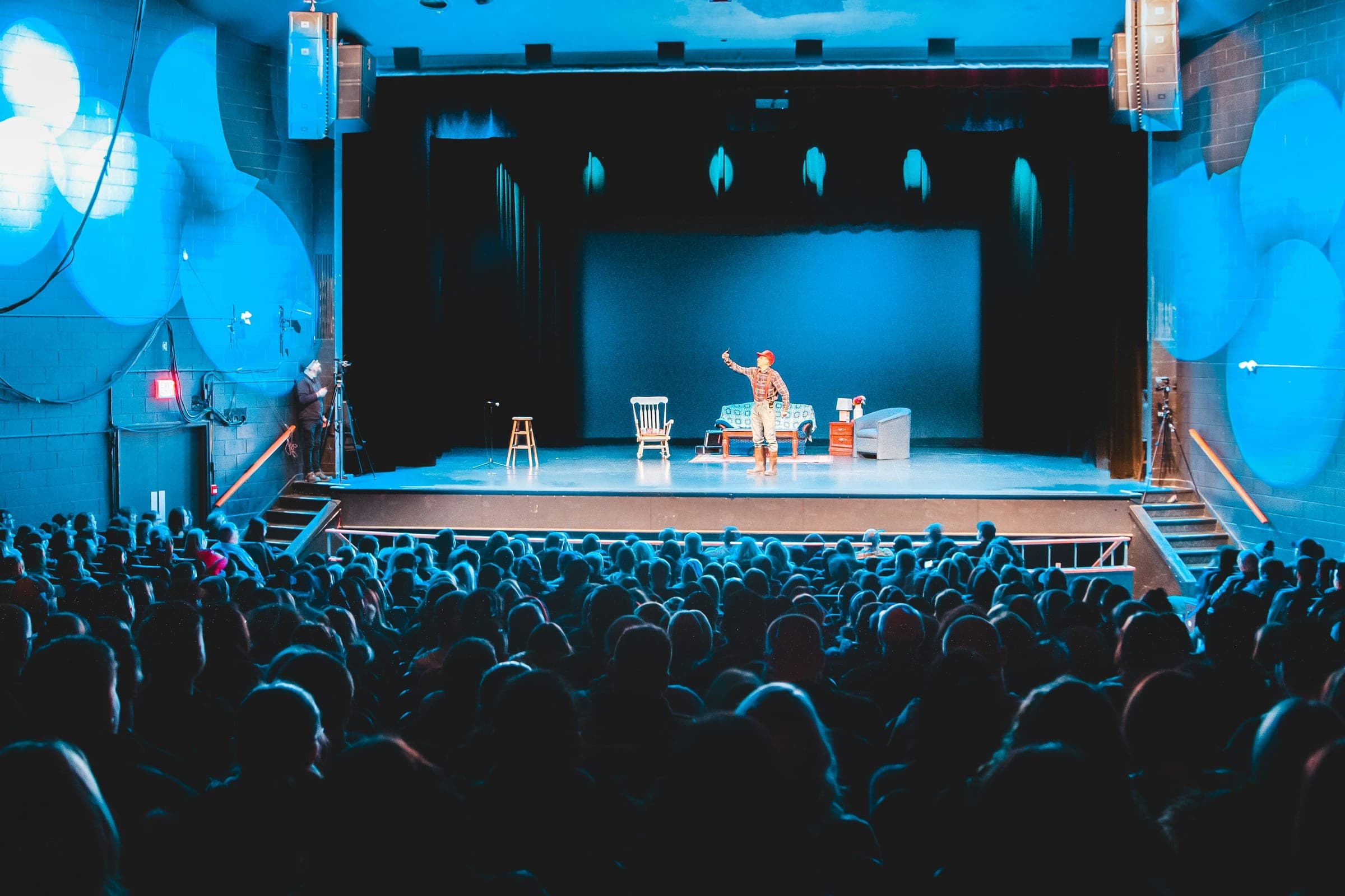 A performer on stage under blue lighting, playing to a packed room