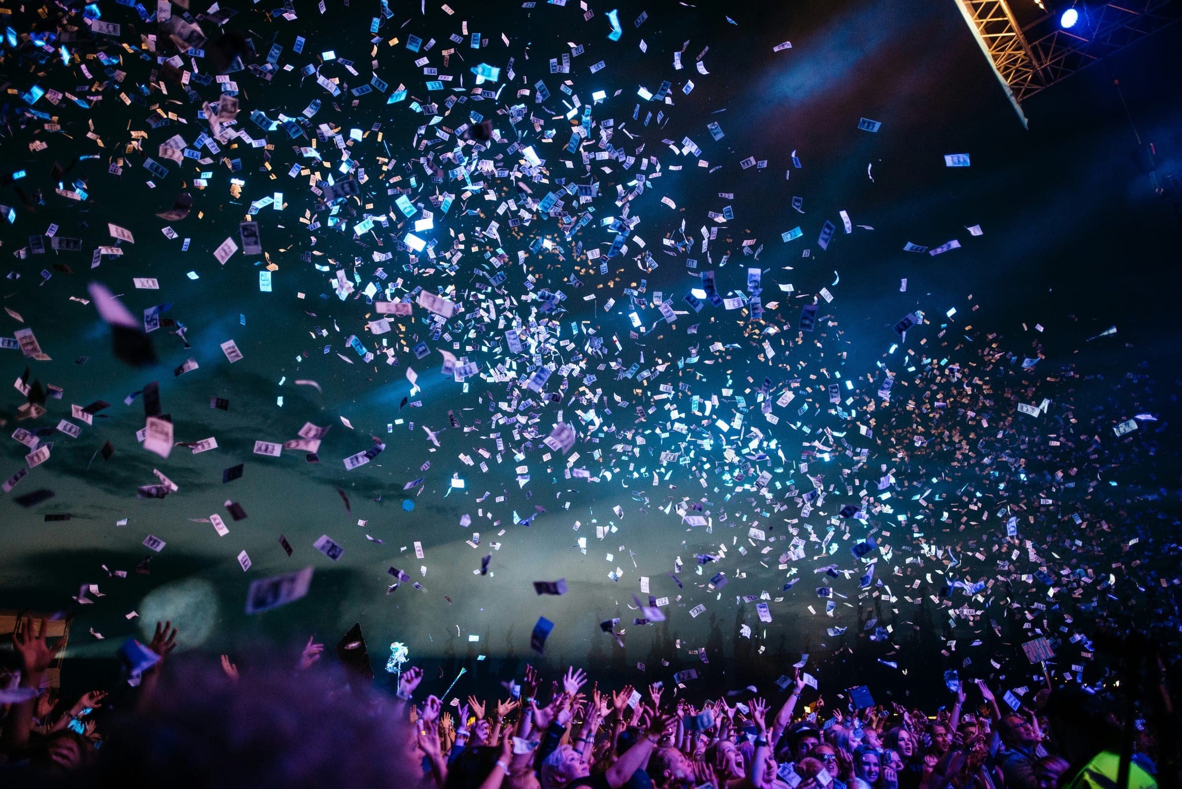 A crowd with hands raised under a shower of confetti at a concert
