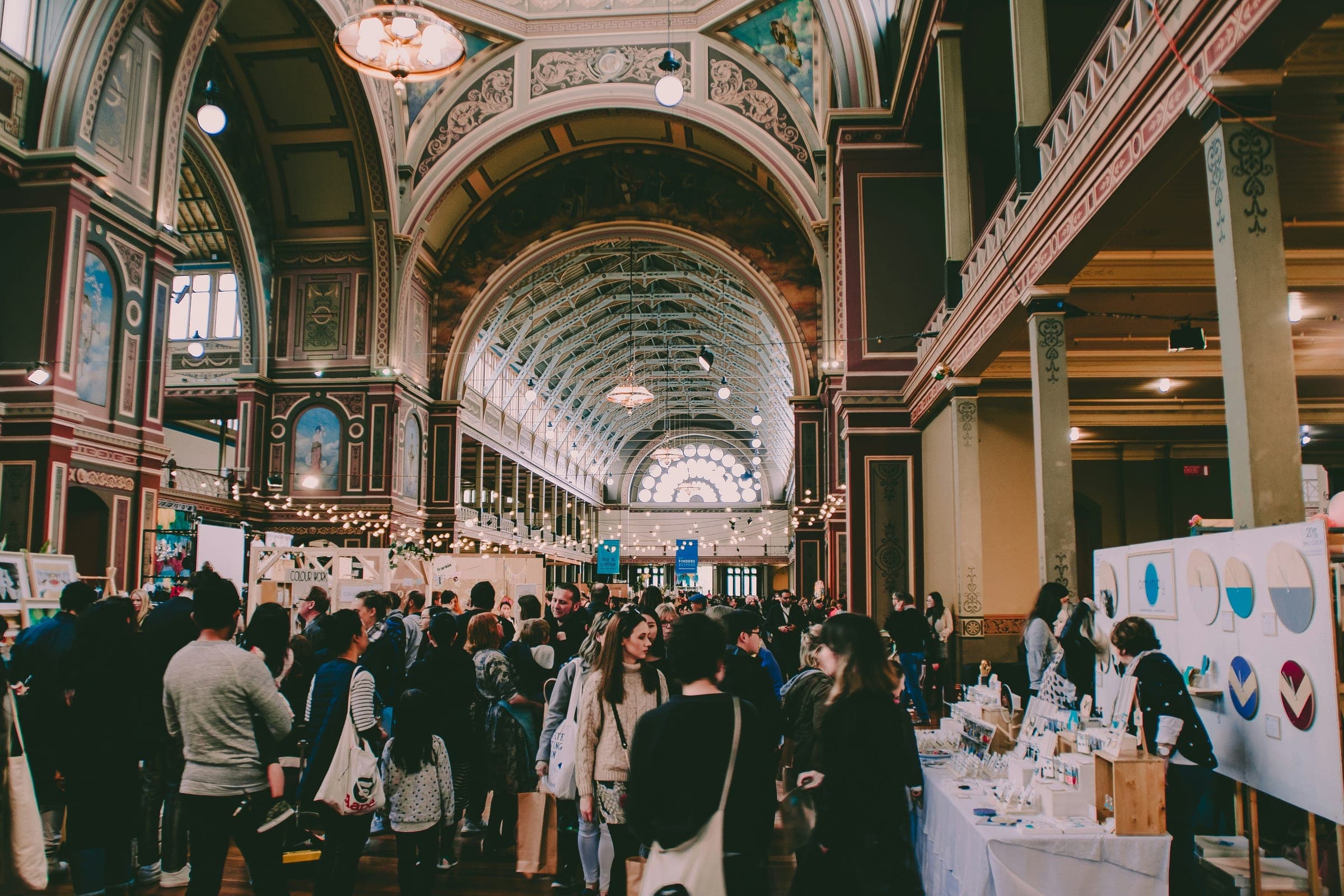 Visitors browsing stalls at a craft market inside a grand exhibition hall